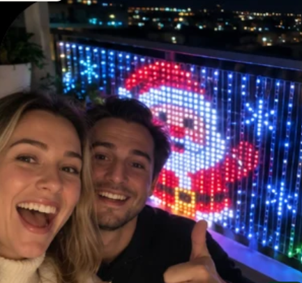 Couple taking a selfie in front of a Santa design on Merrilume lights